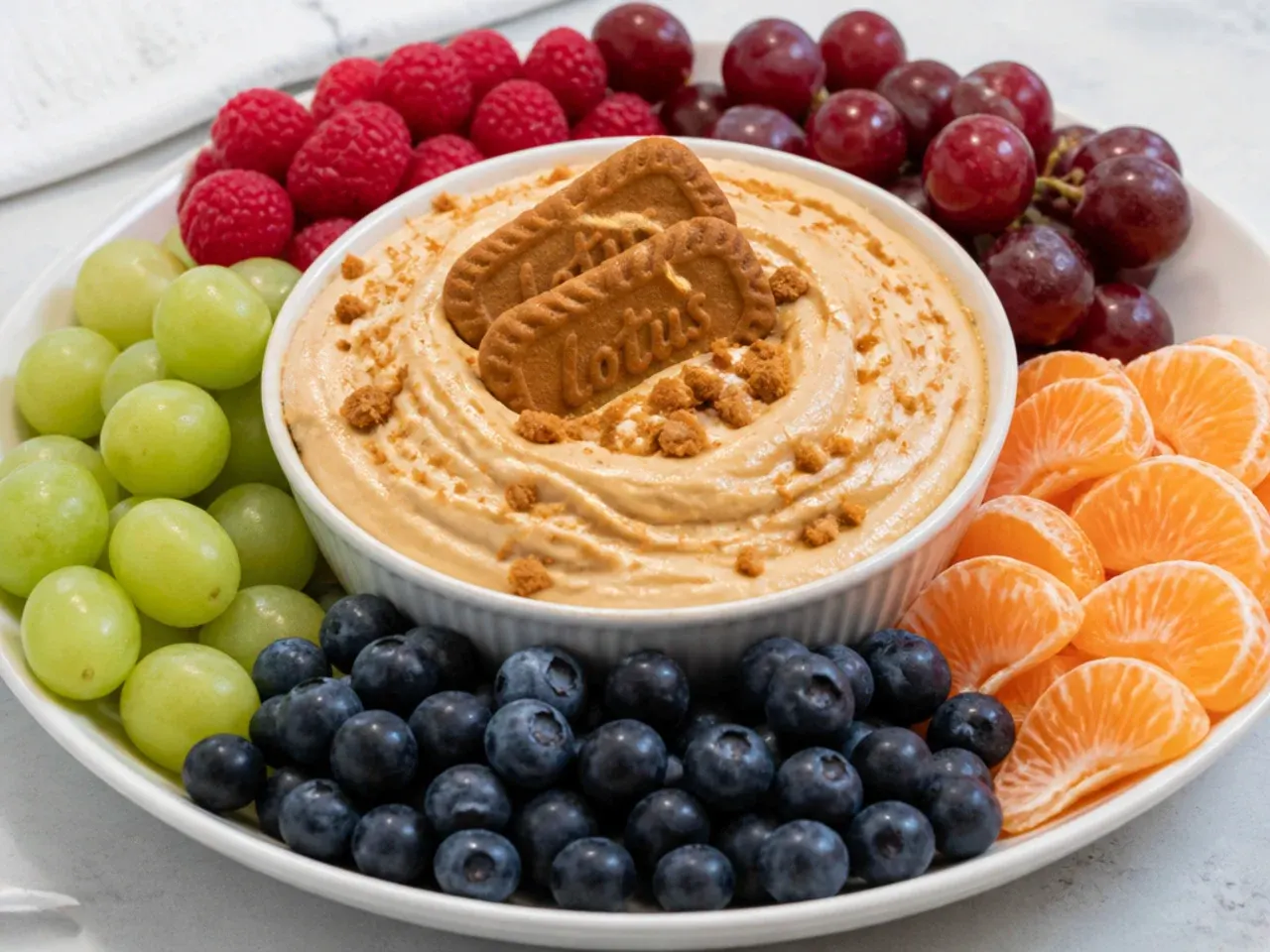 Colorful biscoff cheesecake dip ringed with raspberries, grapes, mandarins, and blueberries