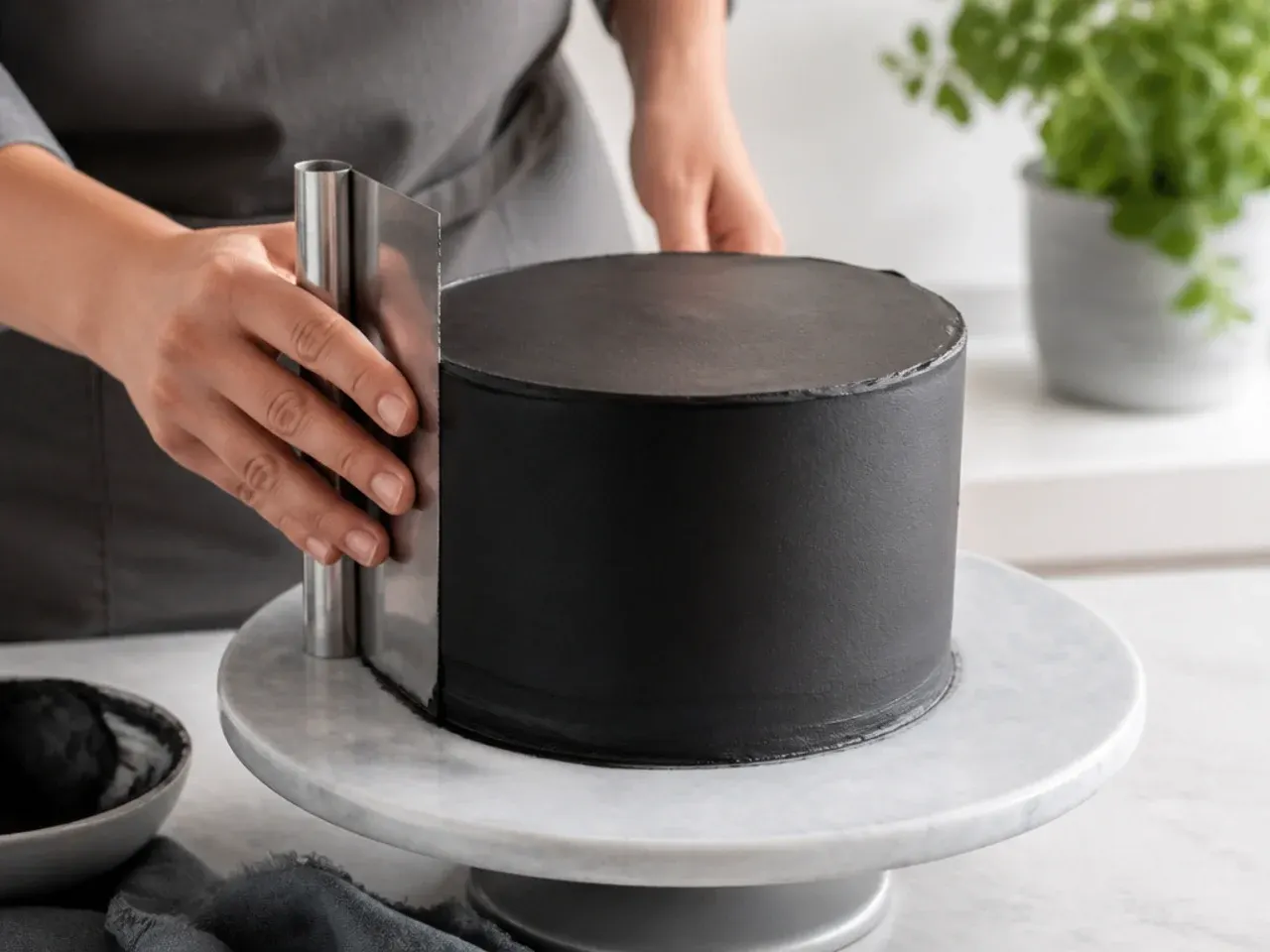 Baker smoothing black buttercream on a birthday cake with a bench scraper