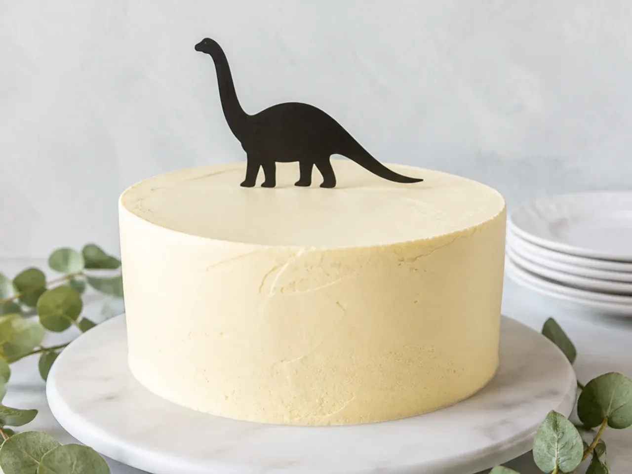 Minimal single dinosaur silhouette cake topper on smooth muted buttercream