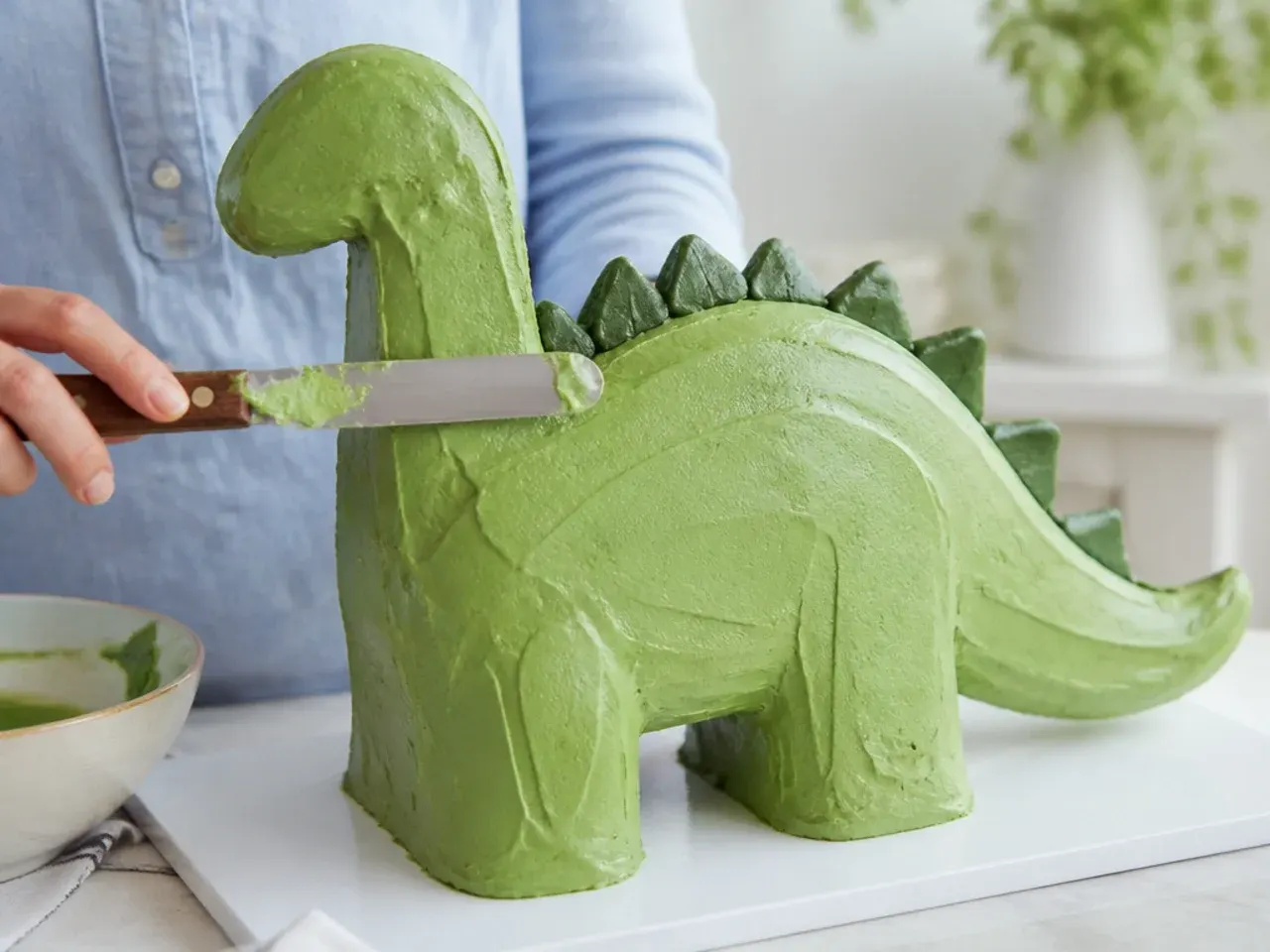 smoothing green buttercream on a homemade dinosaur cake to avoid common mistakes