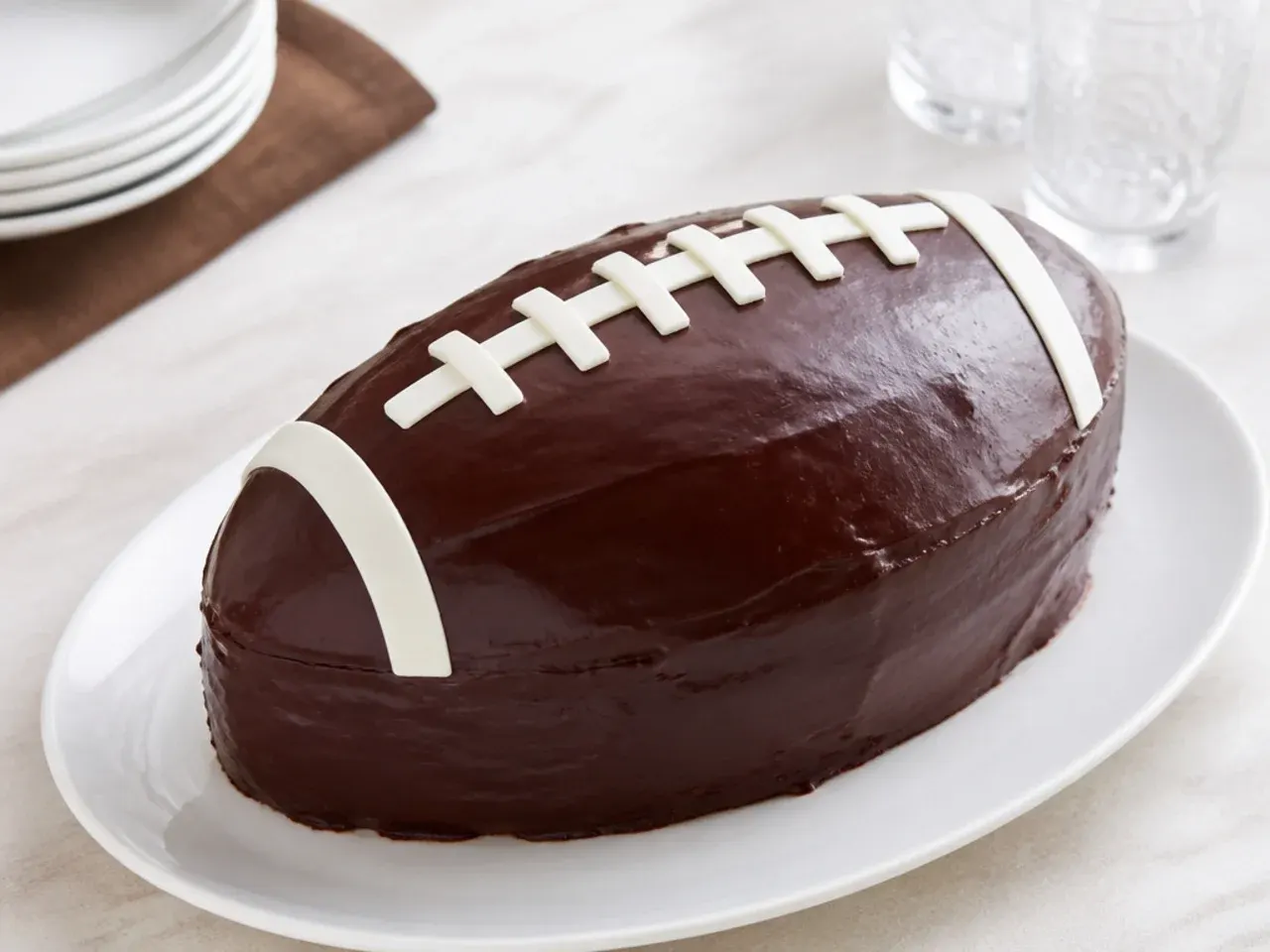 Elegant football cake covered in glossy dark chocolate ganache with white chocolate laces