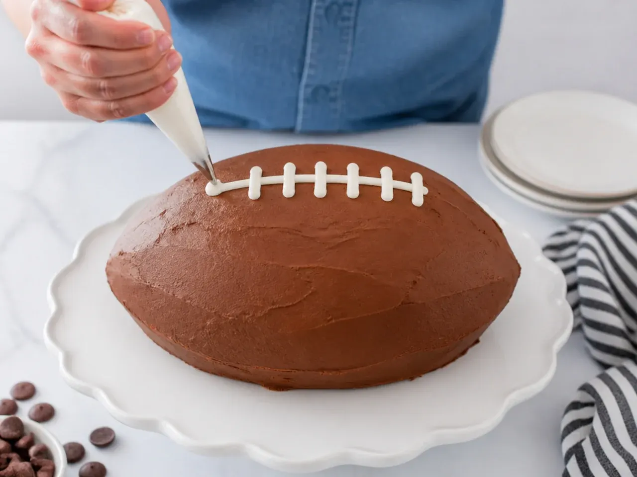 Baker piping white laces onto an easy football cake using a simple piping bag