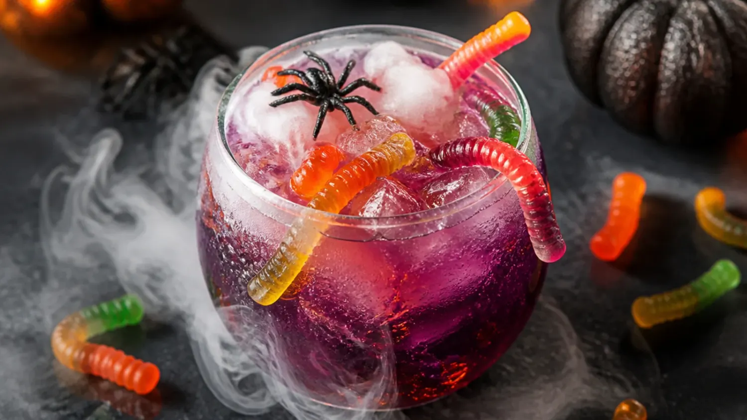 A bubbling green witches' brew Halloween punch in a black cauldron bowl surrounded by orange and purple Halloween drinks on a dark table