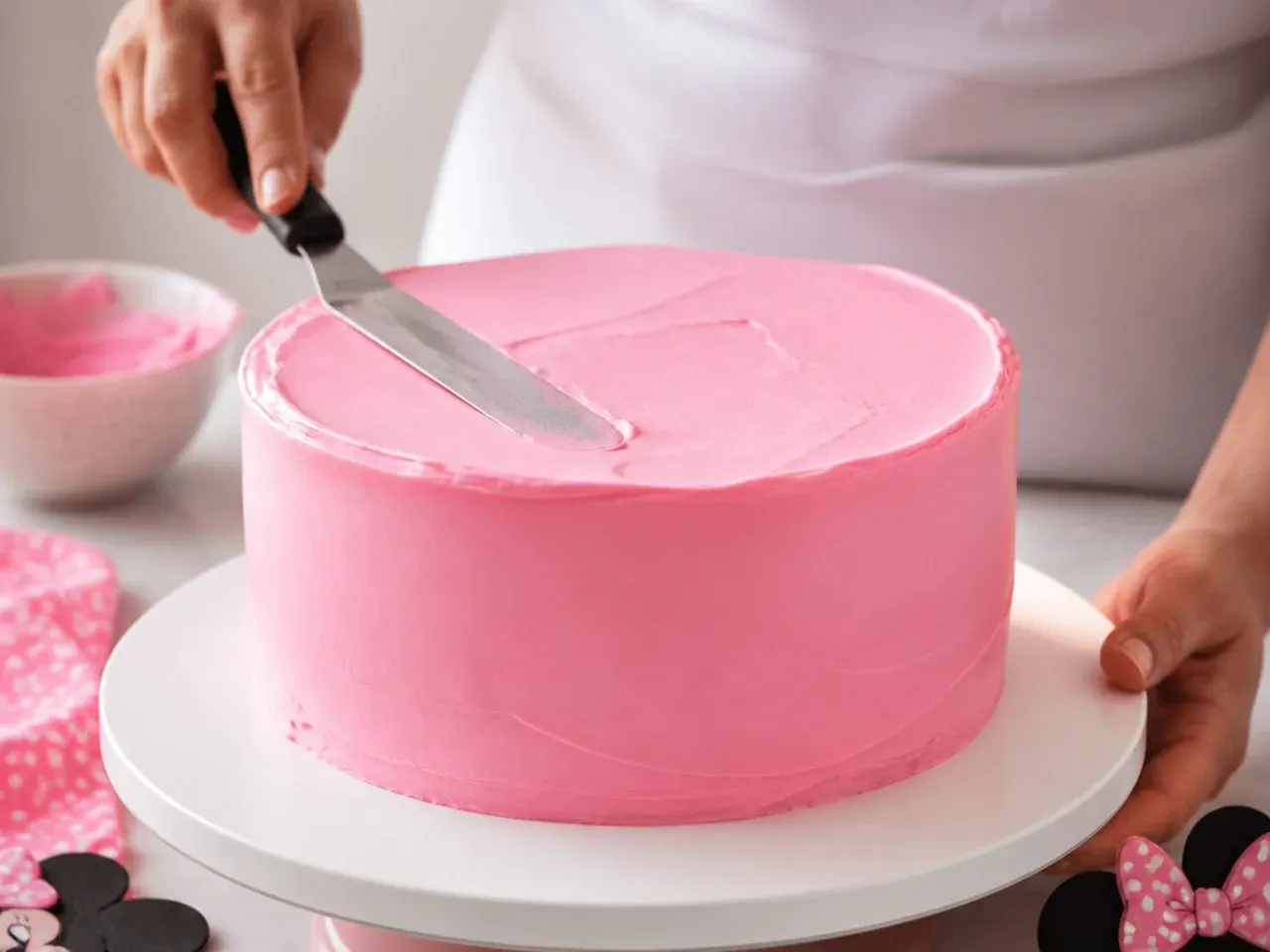 Smoothing pink buttercream on a homemade Minnie Mouse cake