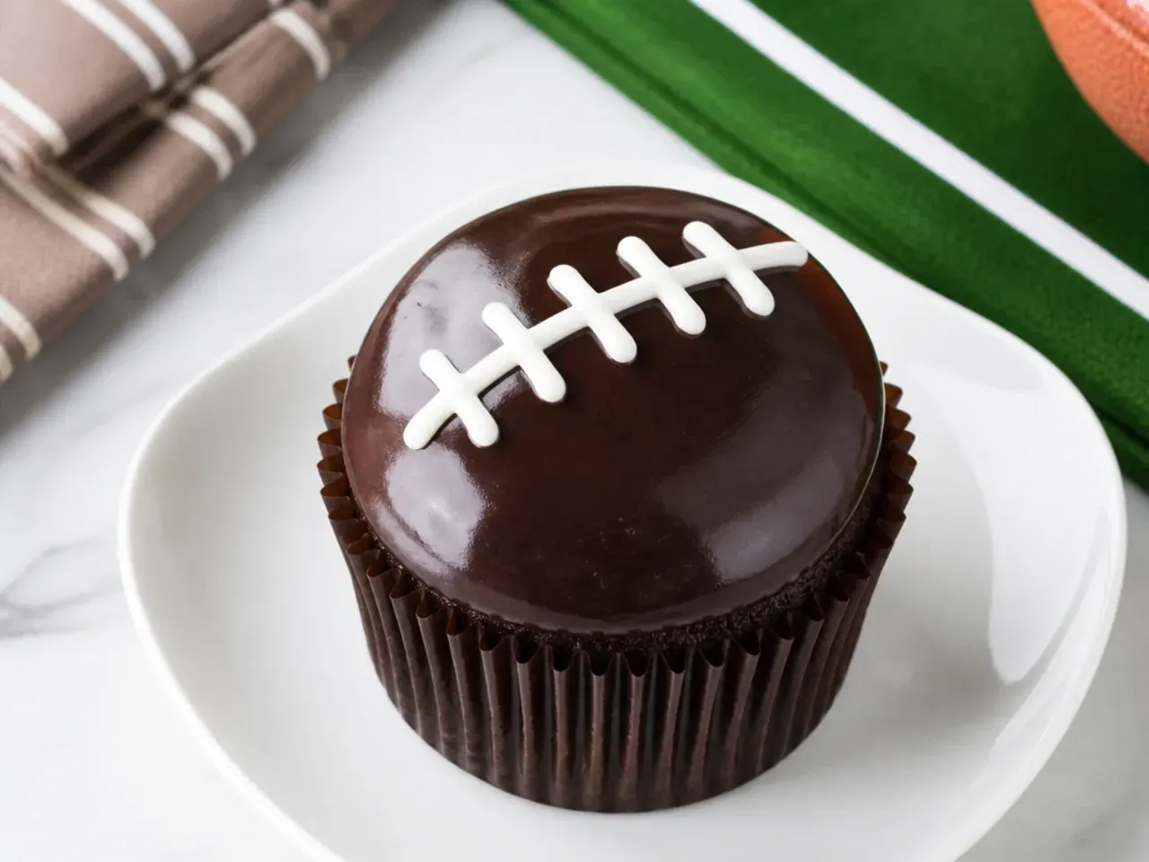 Elegant football cupcakes glazed with dark chocolate ganache and thin white laces