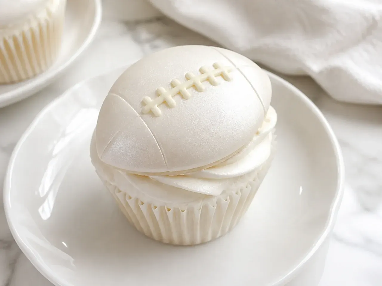 Delicate white-on-white football cupcakes with pale ivory laces and pearl luster dust