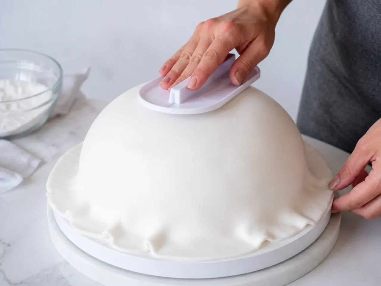 Pro tips for a football fondant cake, smoothing white fondant over a domed sponge with a fondant smoother
