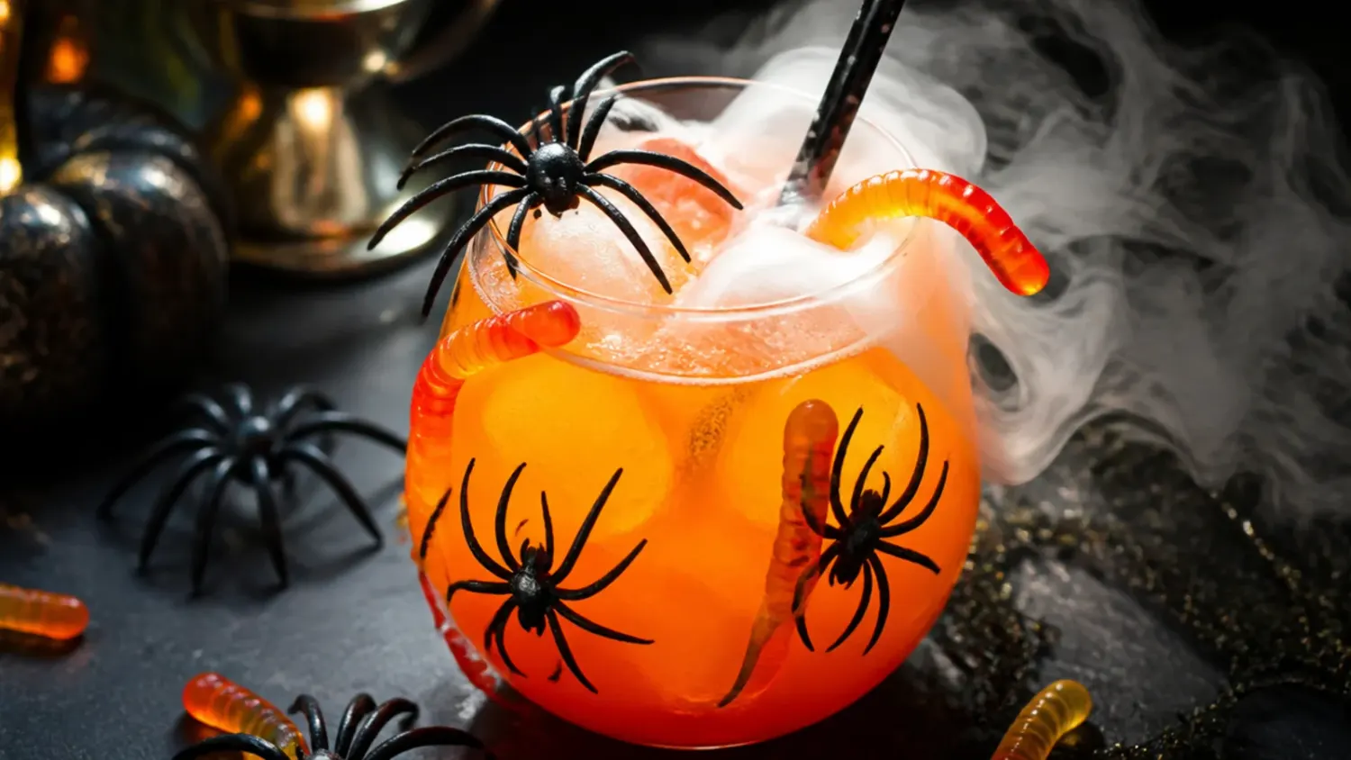 A black cauldron-shaped punch bowl filled with glowing green witches' brew Halloween punch, garnished with lychee eyeballs and surrounded by other Halloween drinks on a spooky party table.