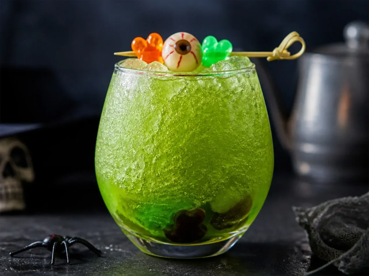 A thick green frozen slush in a glass with gummy frogs perched on the rim.