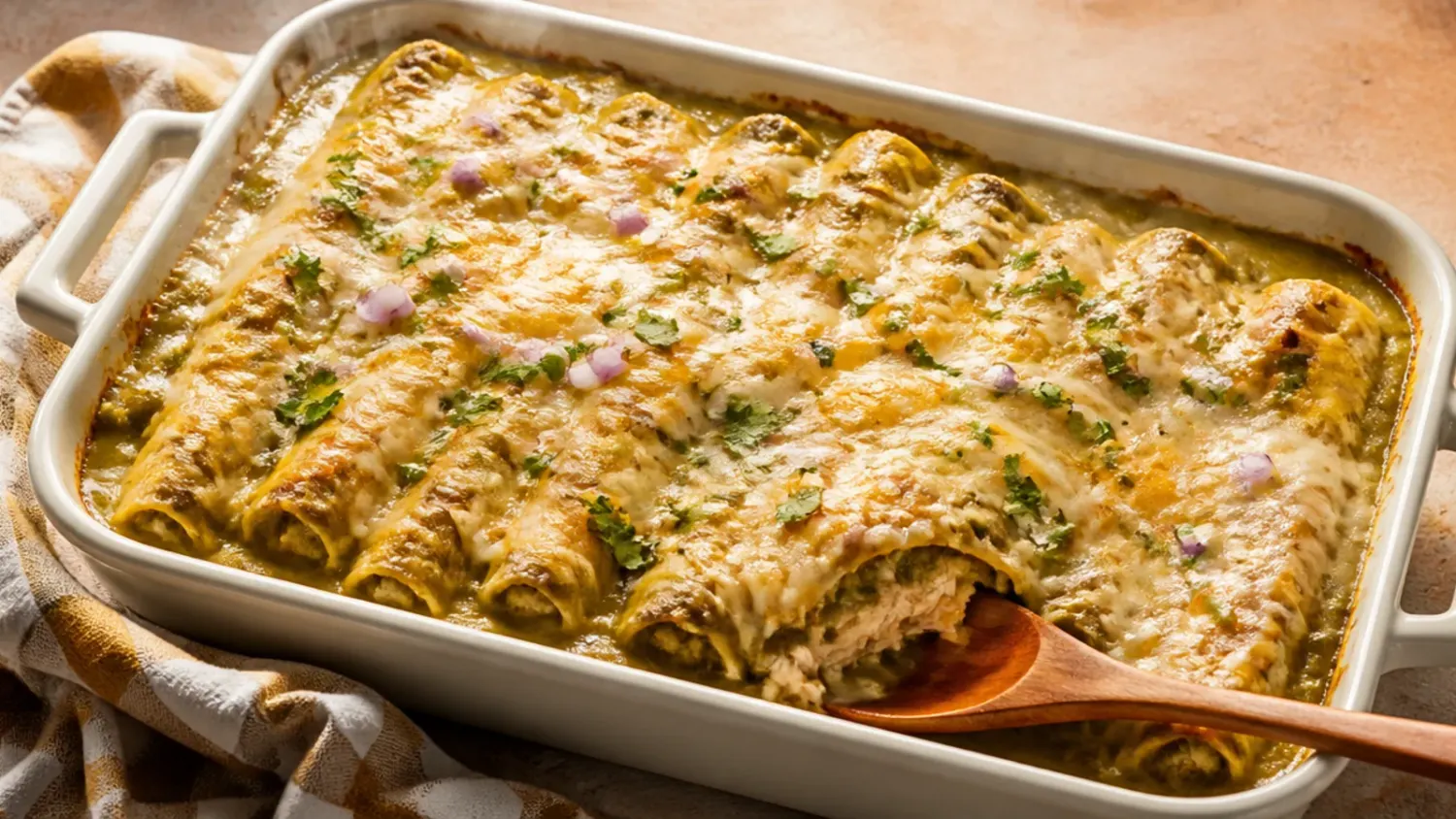 Overhead shot of a bubbling green chile chicken enchilada casserole in a white baking dish, topped with melted cheese, sour cream, chopped coriander and sliced green chiles