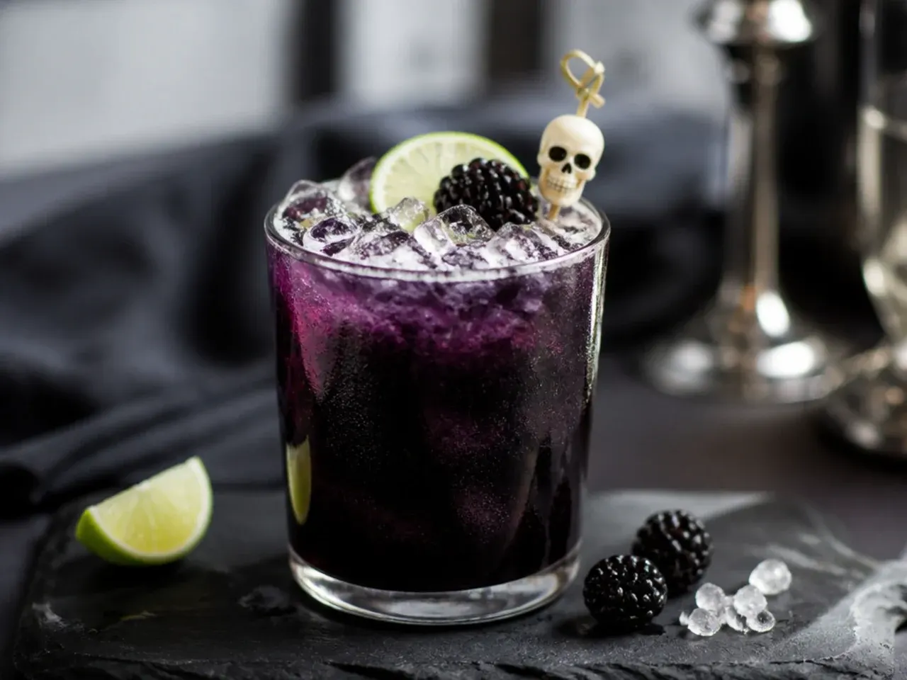 Halloween drinks table with garnish trays of gummy worms, candy eyeballs, ice cube trays and paper straws.