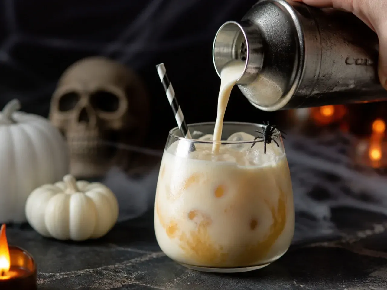 Creamy pale pink Halloween milk punch in a small glass with a black food-gel spiderweb swirl on top