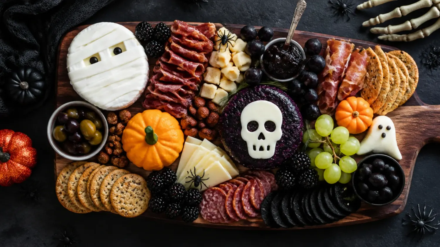 A rustic wooden platter styled as a halloween themed charcuterie board with orange and black meats, cheeses and a spider web dip