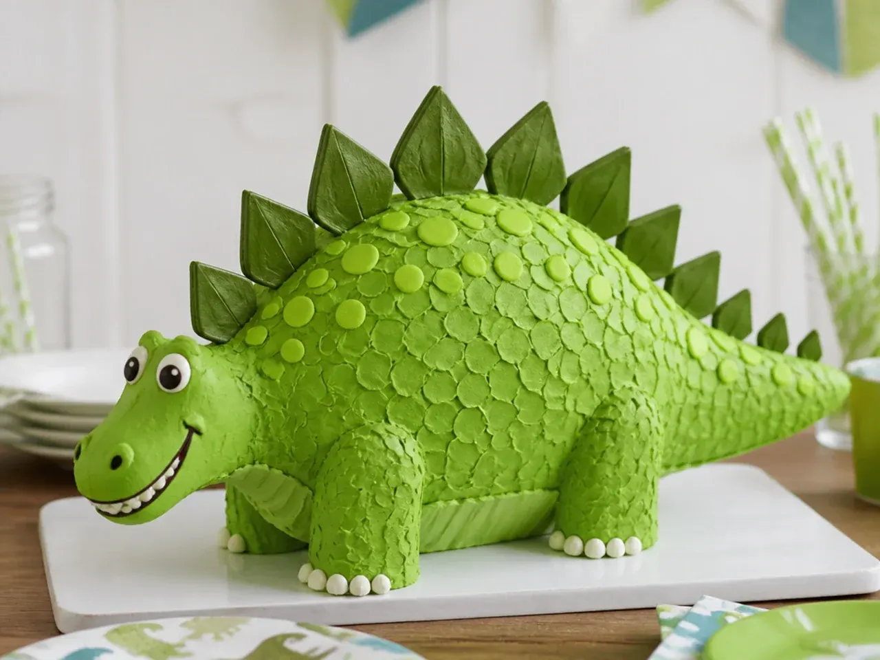 Finished homemade dinosaur cake with green scales, spikes, and a friendly smile on a party table