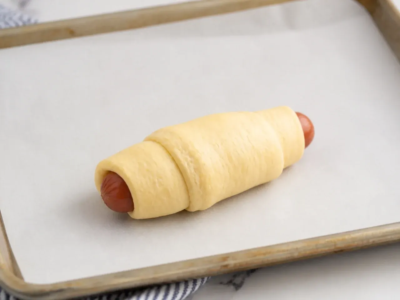 Crescent dough rolled snugly around a sausage and placed seam-side down for homemade pigs in a blanket