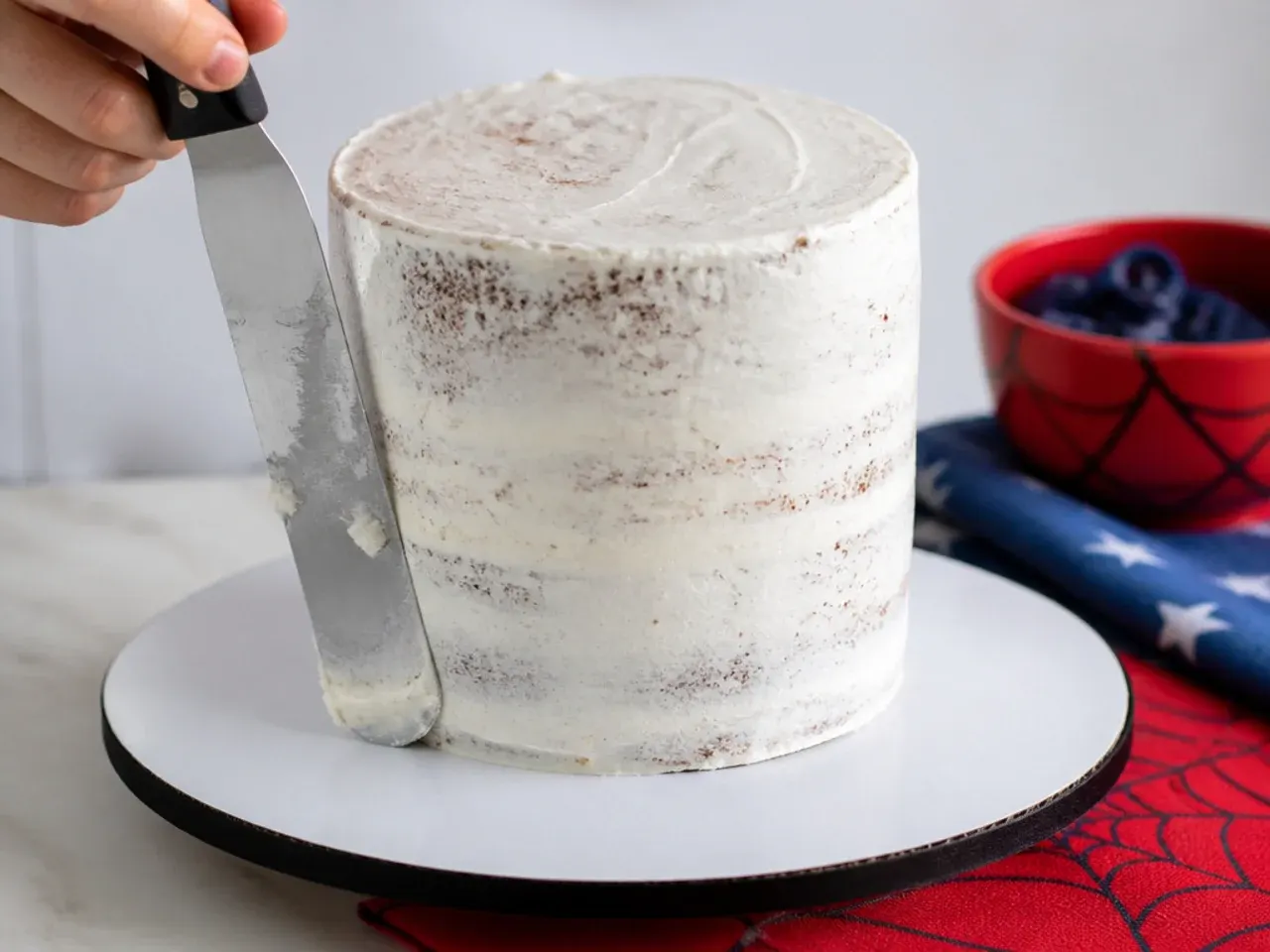 Thin crumb coat scraped over a stacked homemade Spiderman cake before the red frosting goes on
