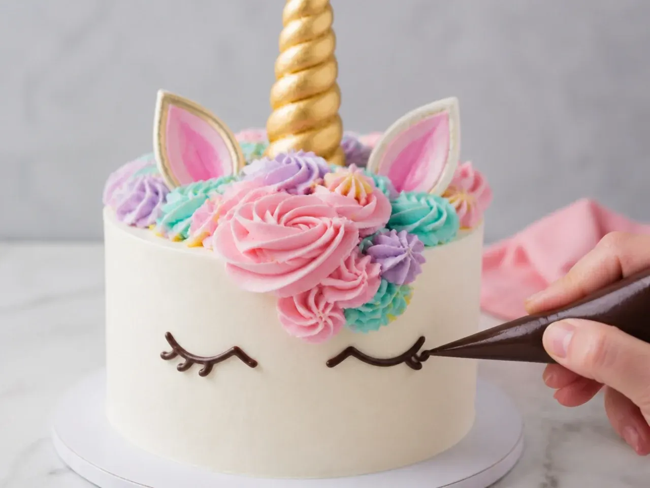 Piping closed chocolate eyes with curled lashes on an easy unicorn cake