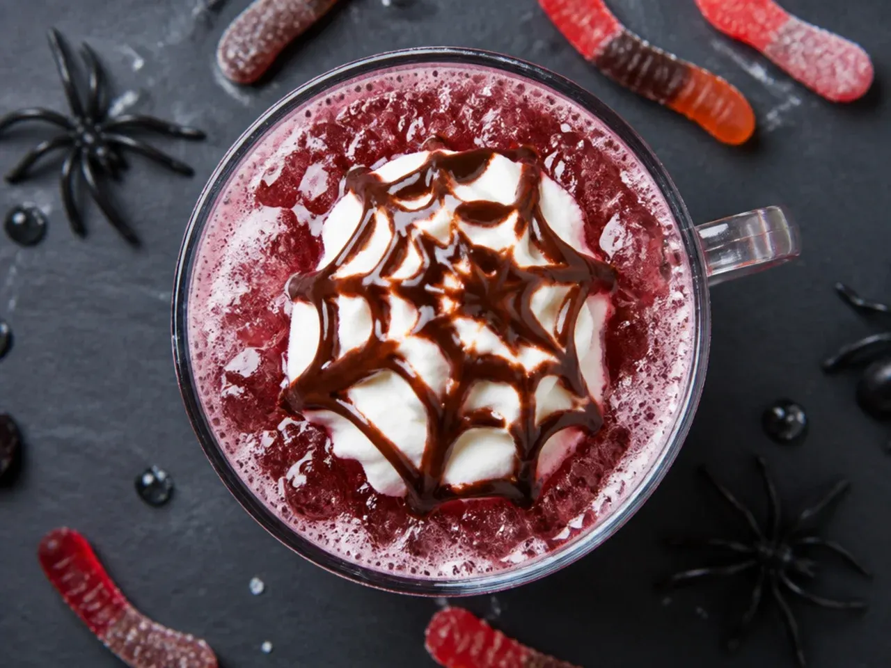 Fruit punch bowl with a white chocolate spider web design on top for kid friendly halloween drinks