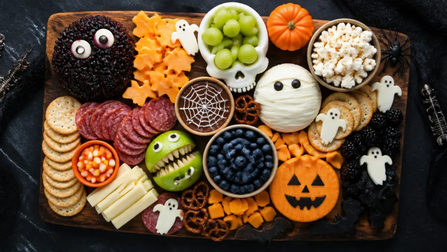 A wooden board arranged for a kids halloween charcuterie board with cheese cubes, banana ghosts, clementine pumpkins and pretzel sticks