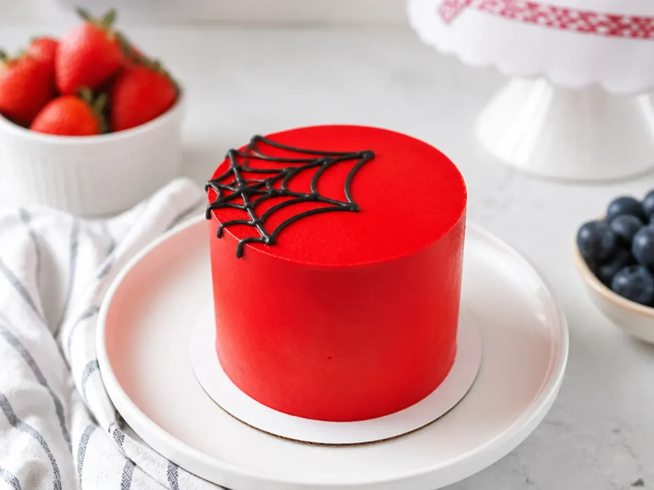 Minimal red mini spiderman cake with a single delicate web in the corner