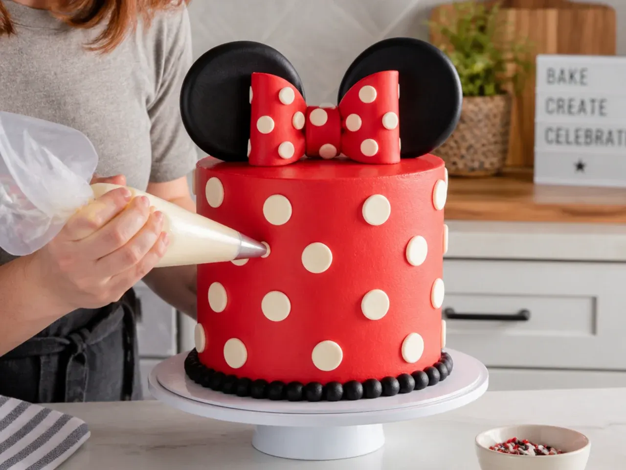 Home baker piping buttercream polka dots on a Minnie Mouse inspired cake at the kitchen counter