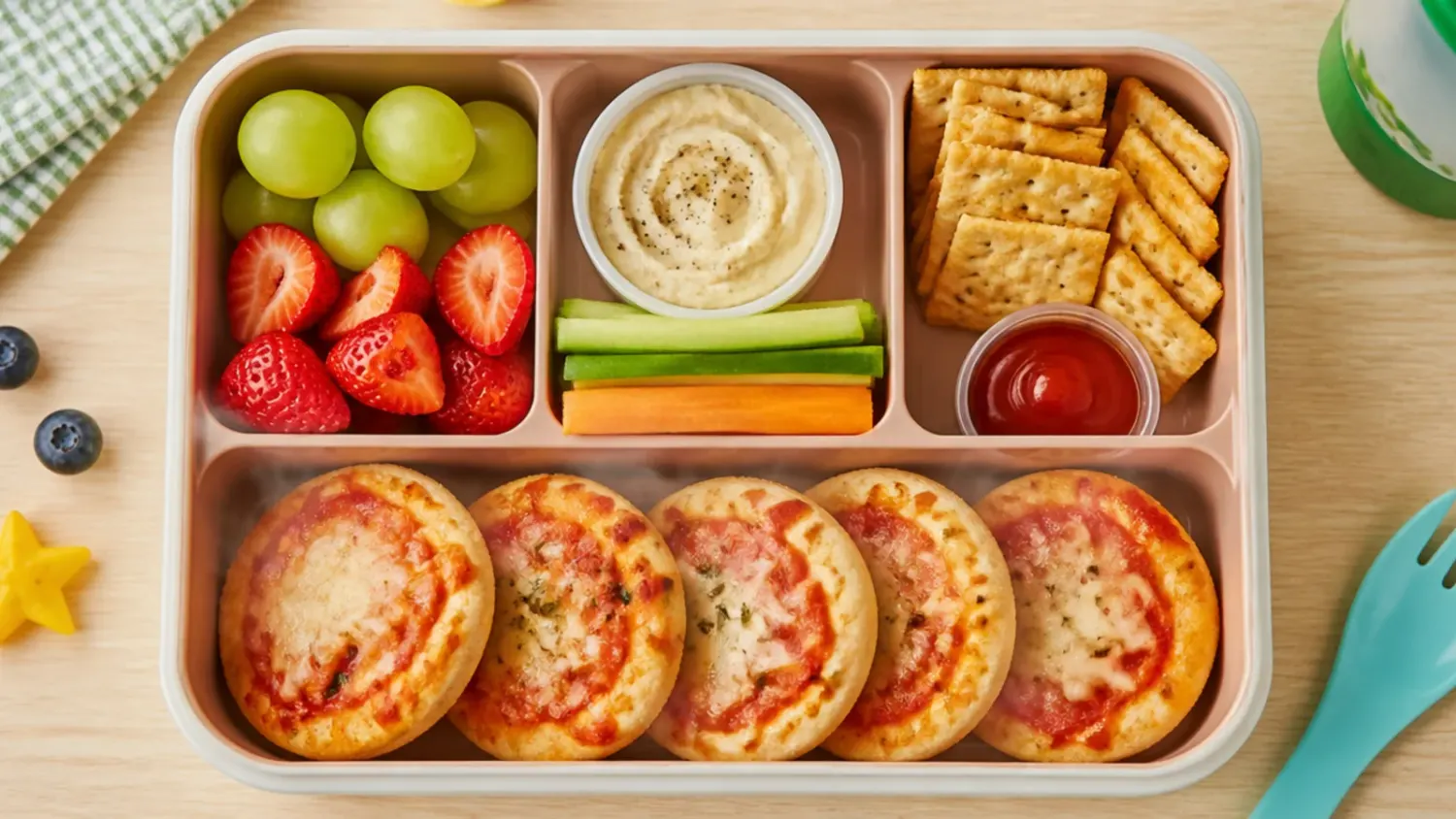Overhead shot of a picky-eater-friendly lunch box with ham and cheddar muffins, cheese cubes and fruit kept in separate compartments