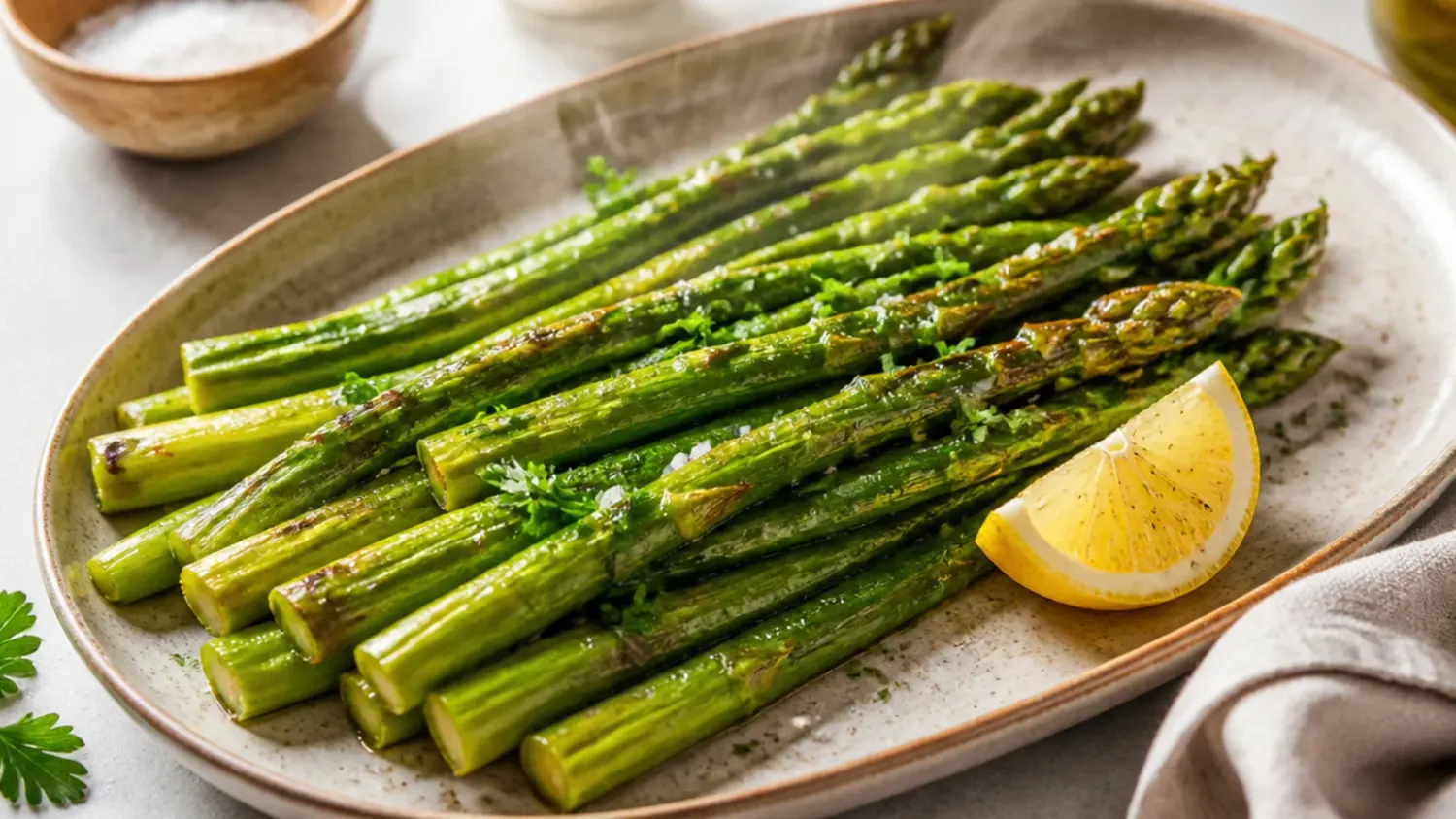 Overhead shot of golden roasted asparagus spears topped with Parmesan and lemon on a white platter