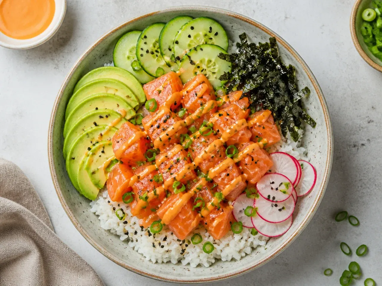Overhead flat lay of a salmon sushi bowl with seasoned rice, avocado, cucumber and sriracha mayo