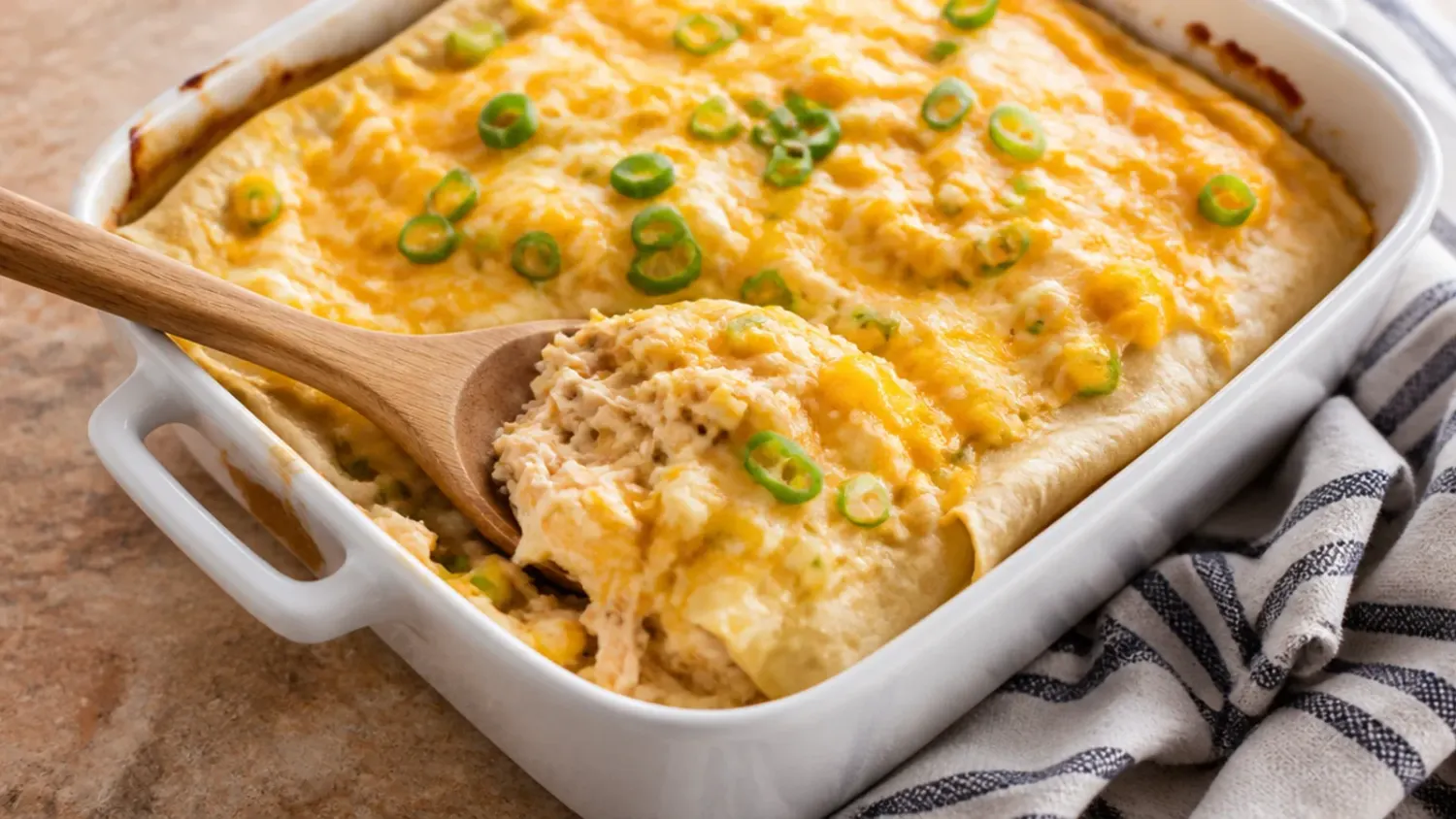 Overhead view of a baked sour cream chicken enchilada casserole in a white dish, melted cheese pulling apart with coriander and diced tomato scattered on top