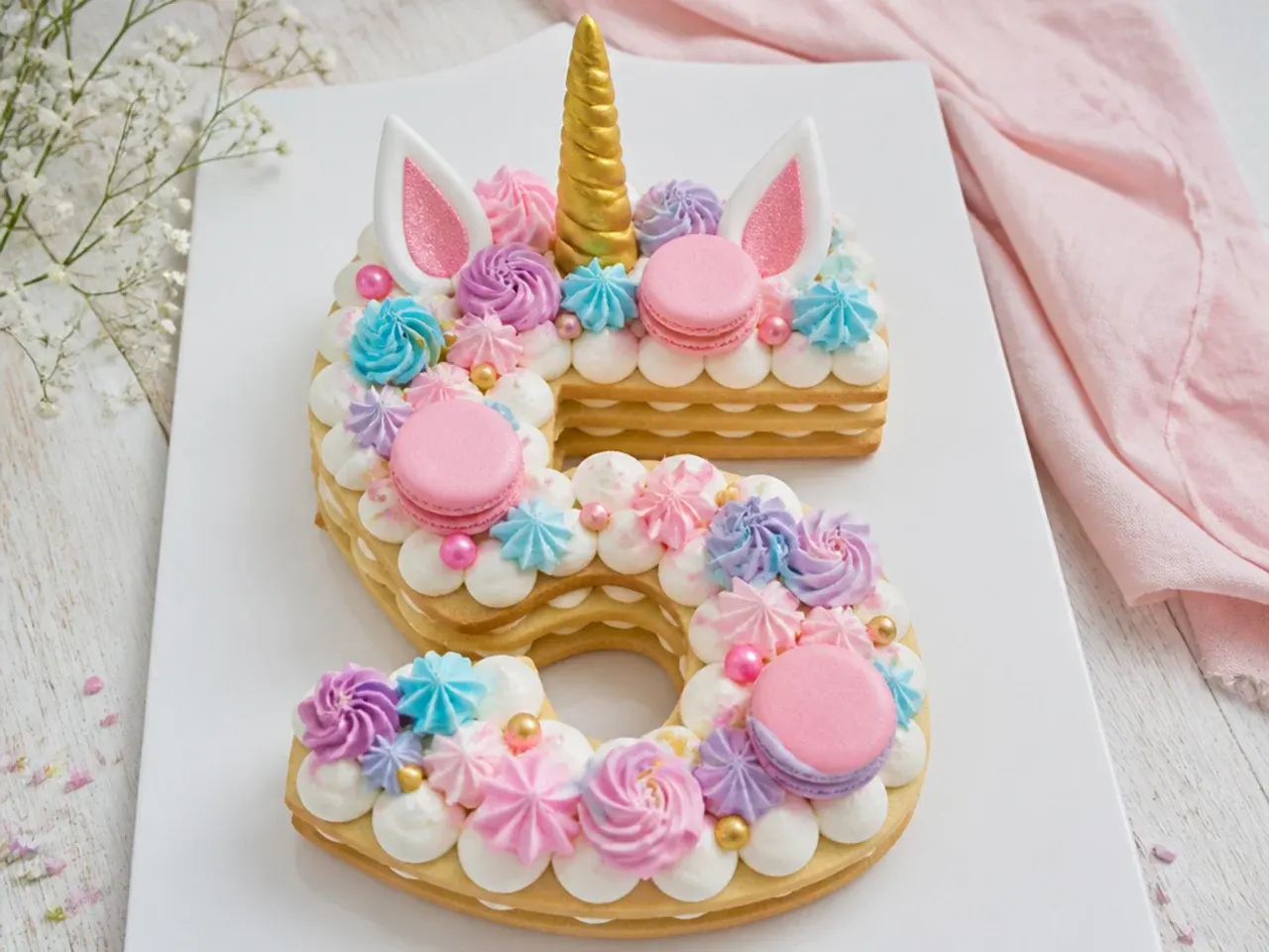 Whimsical unicorn number cake decorated with meringues and macarons