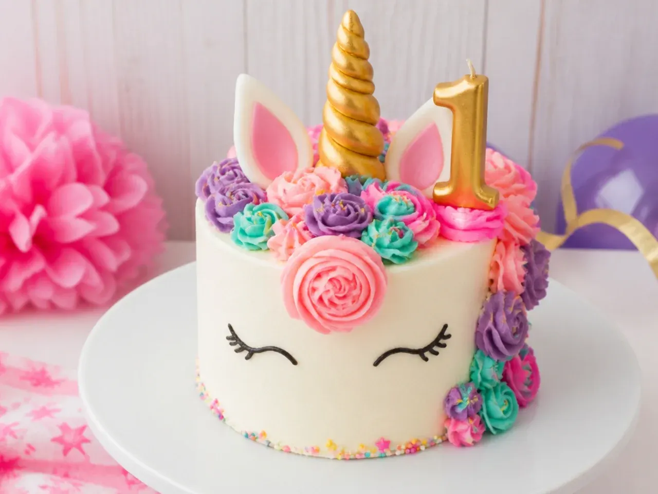Festive unicorn smash cake with a gold number one candle for a first birthday